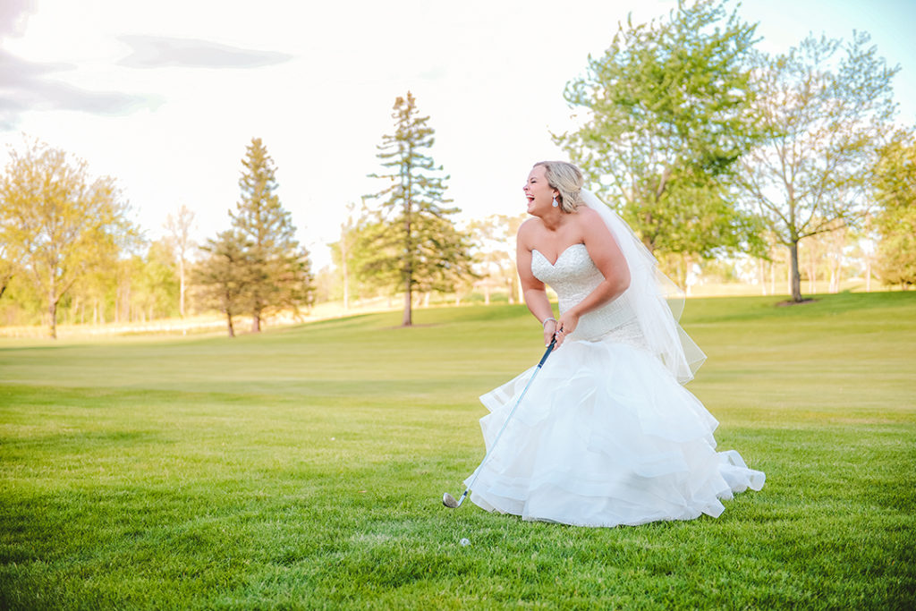 the bride laughing as she tries to hit a golf ball in her white wedding dress
