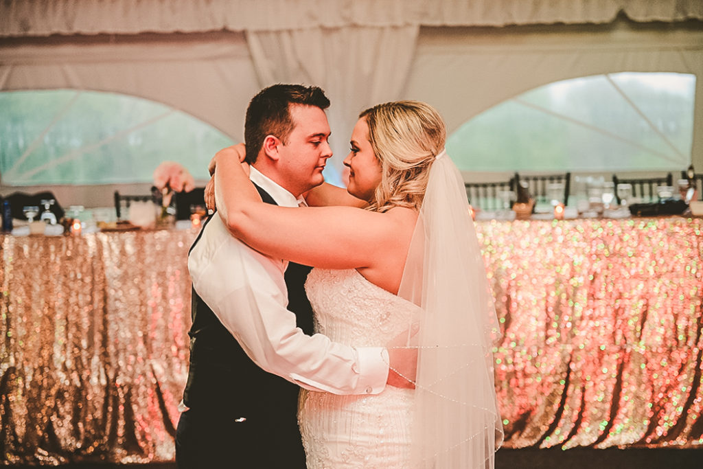 a wedding couple getting close during their first dance in front of the head table with gold glitter
