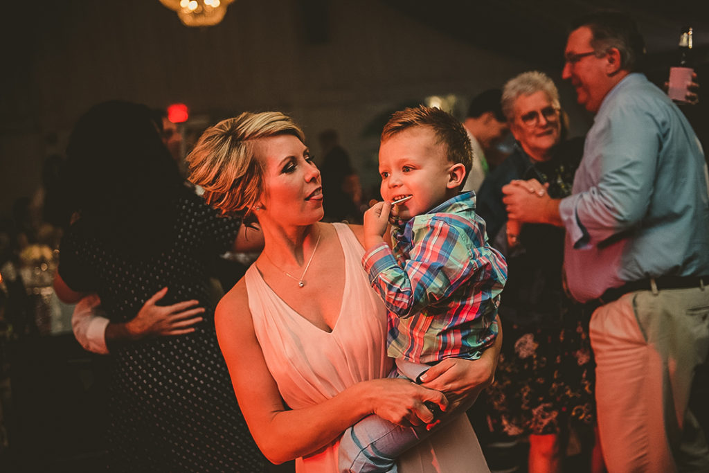 a mom holding her son as they dance on a dance floor in orange light