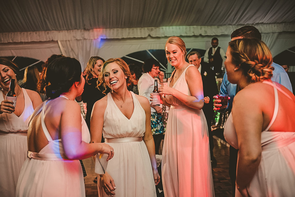 the made of honor laughing as he dances wit the other bridesmaids wearing a pink dress