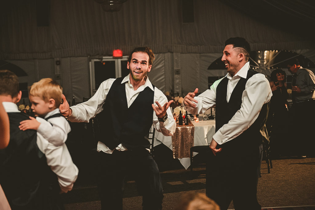 two men making a funny face while they dance at a wedding reception