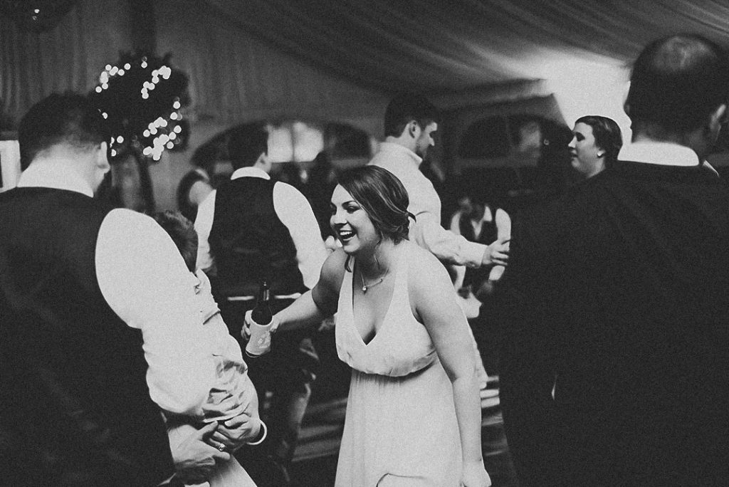 woman dancing at a reception laughing while holding her beer in black and white