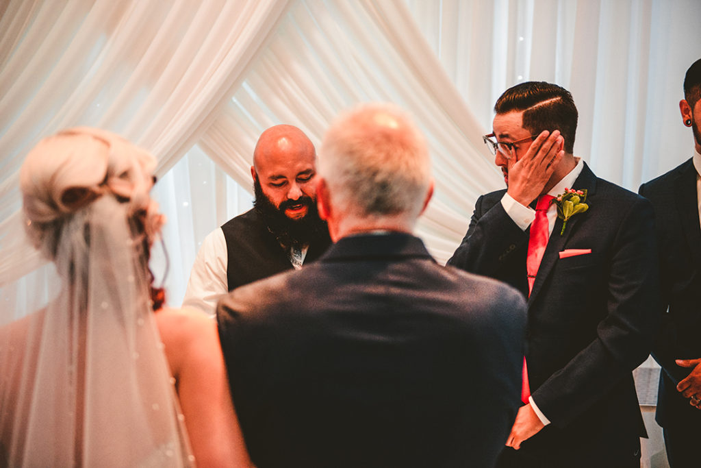 groom wiping away tears after seeing his bride for the first time at his wedding