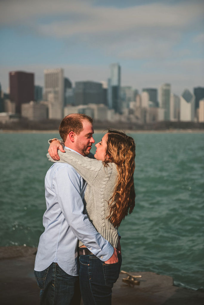 a man warming his hands in his girlfriends back pockets by a cold Lake Michigan