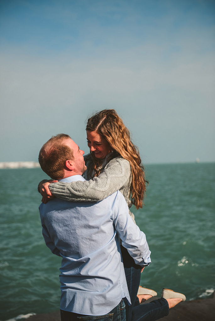 a groom picking up his bride as they laugh and look into each others eyes in front of turquoise water