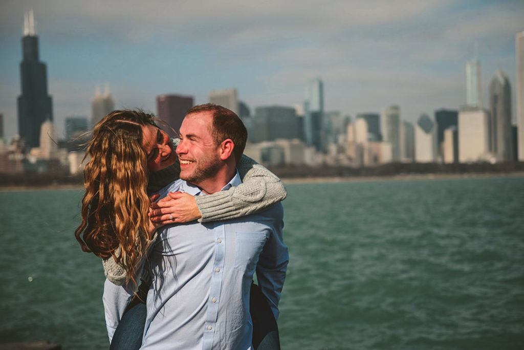 an engaged couple flirting in front of the Chicago skyline in the morning