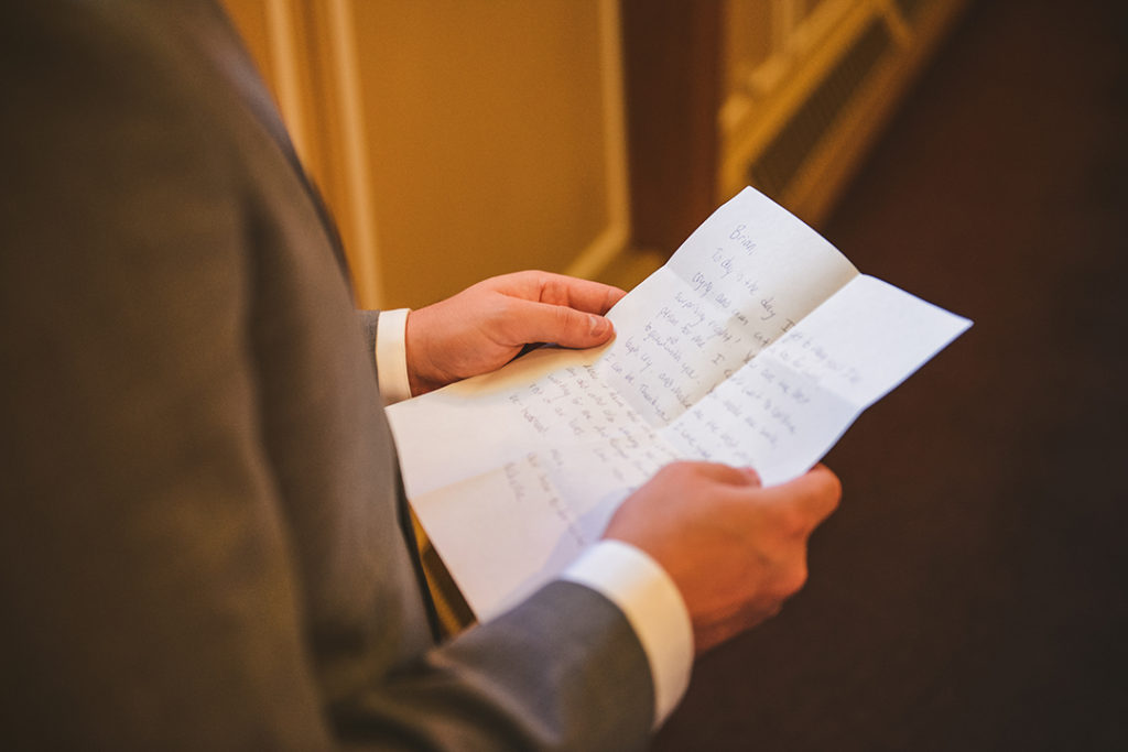 a groom holding onto a note that his bride wrote him at a church