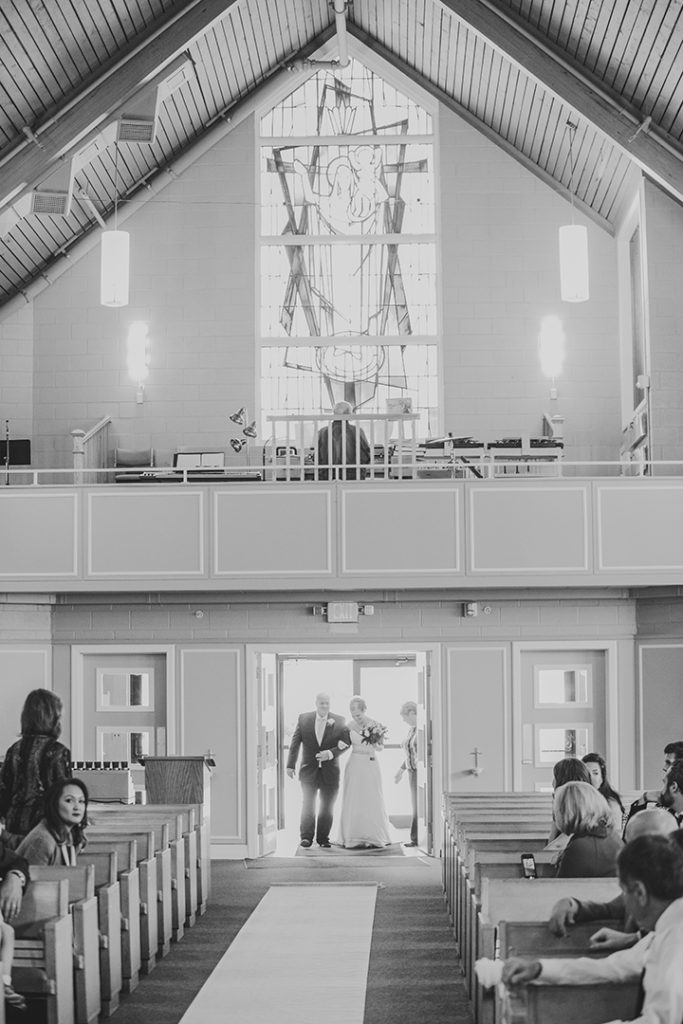 a father and his daughter walking into a church in black and white