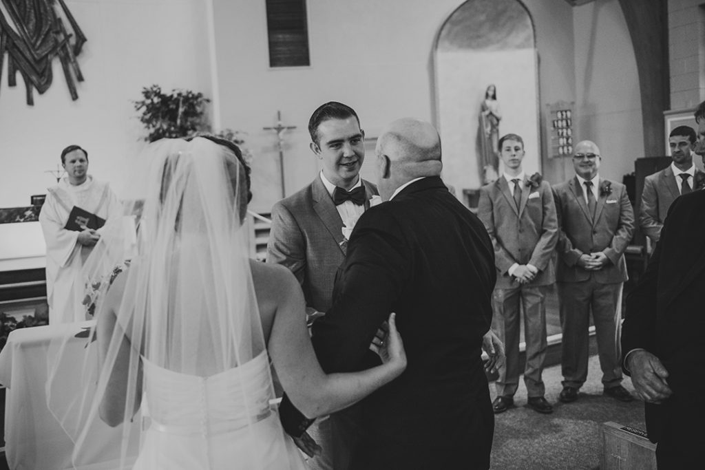 a happy groom as the brides father walks her down the church aisle