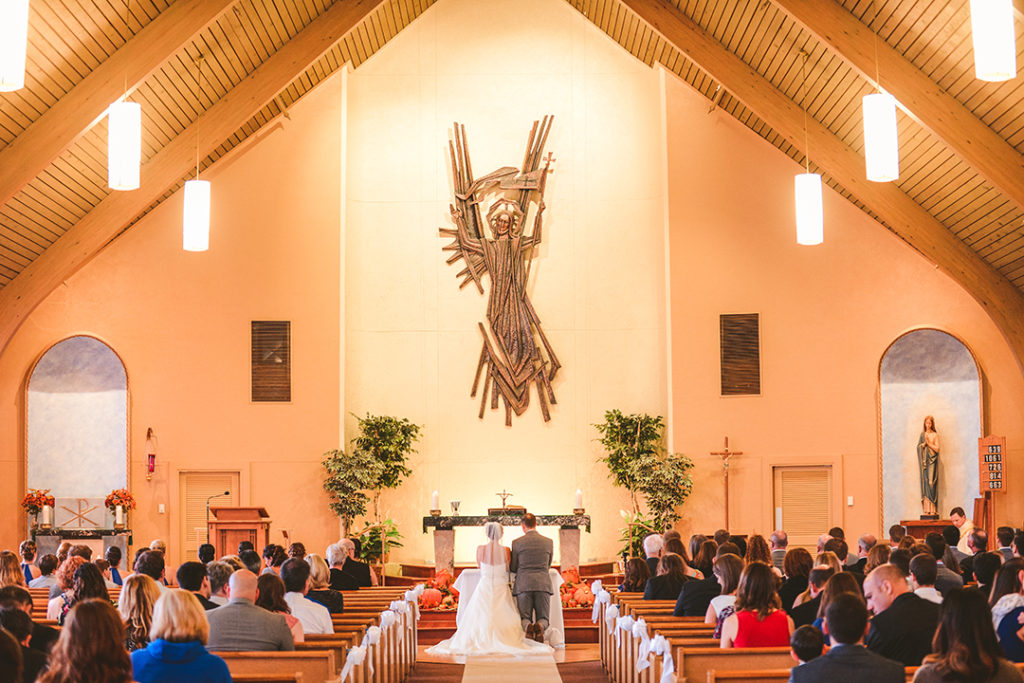 a couple kneeling at a church alter as their friends and family watch