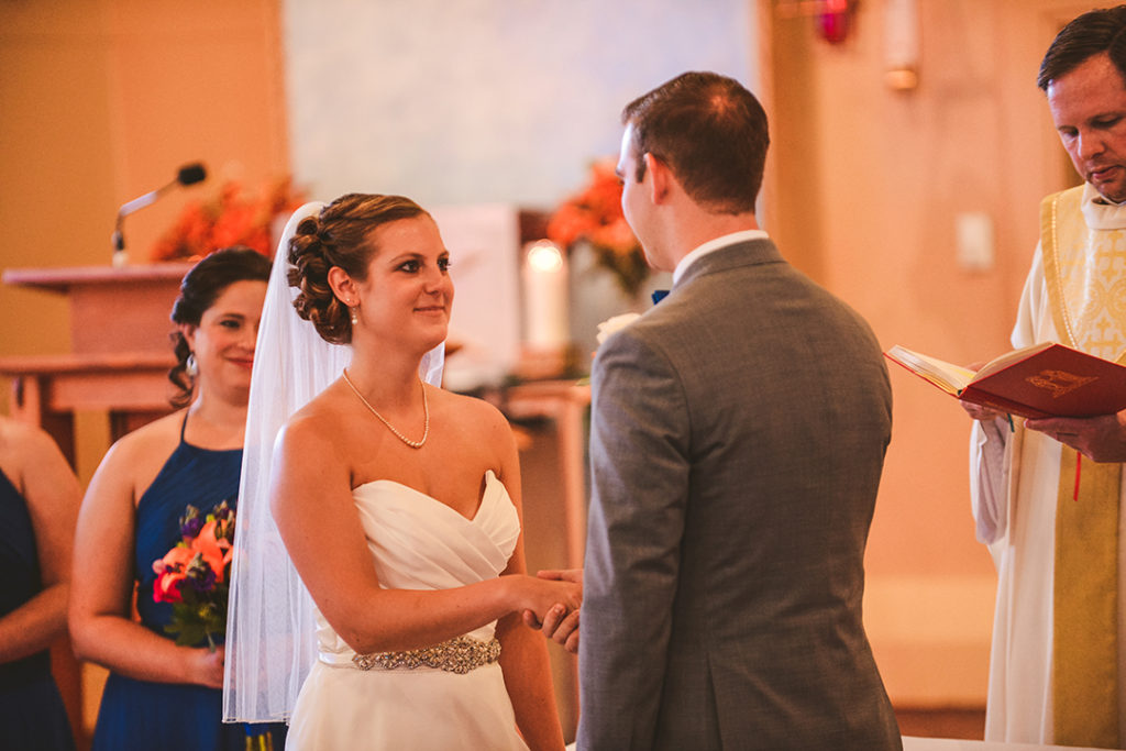 a bride looking at her groom as he holds her hand at the church alter