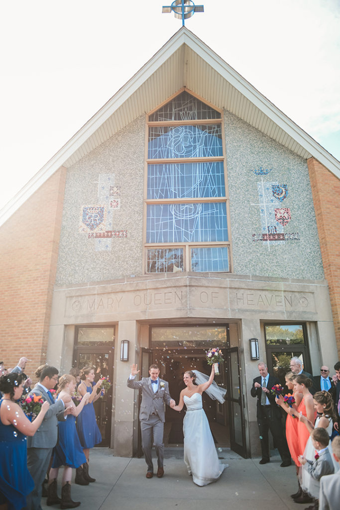 a bride and groom exiting a church to bubbles and cheering wedding guests