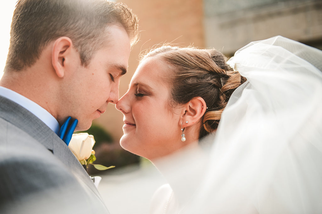 a bride and groom touching noses with the veil coming towards the camera