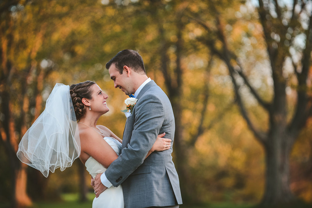 a bride and groom laughing as they look into each others eyes in the woods in the fall