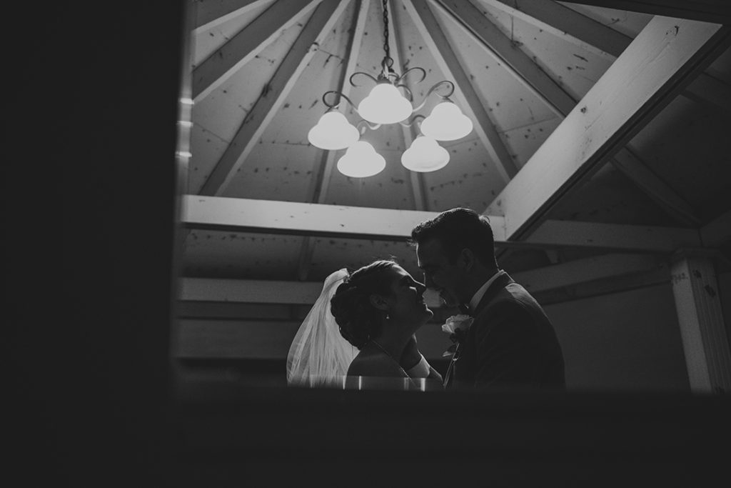 newlyweds sneaking a kiss in a gazebo at night in black and white