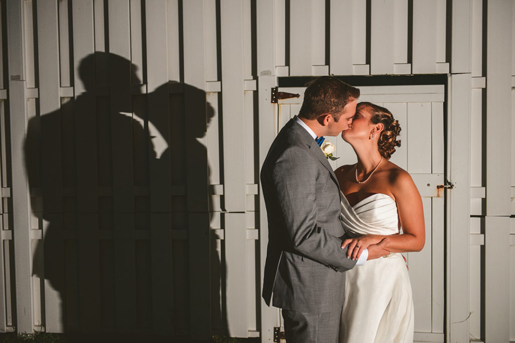 a man and a woman kissing with their shadow on a white fence in the background