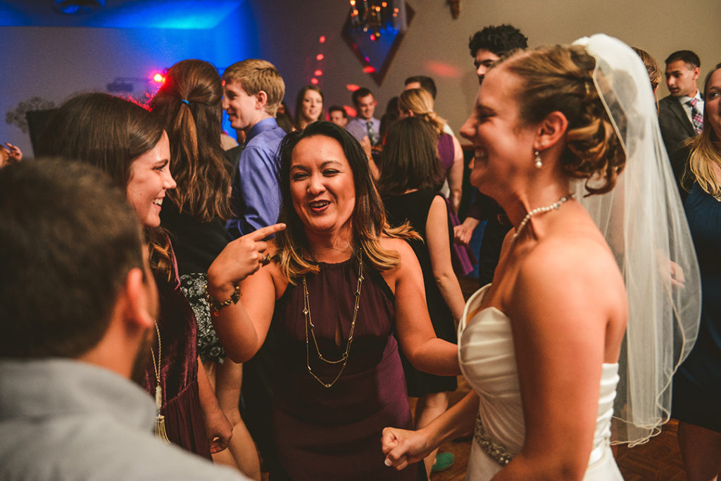 a woman pointing to the bride on a packed dance floor as everyone laughs