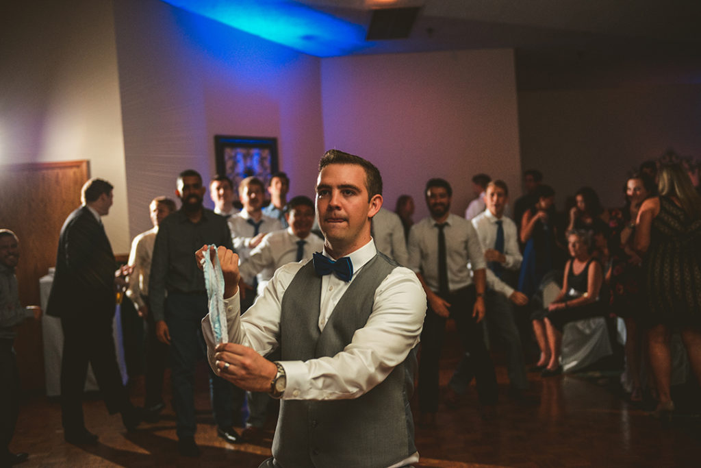 a groom winding up to throw a garter in front of a group of guys getting ready to catch it