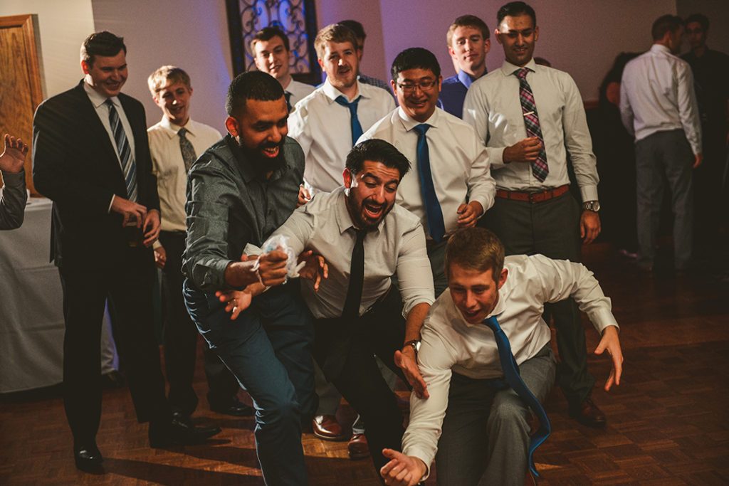 three men fighting over the garter during a wedding reception as everyone laughs