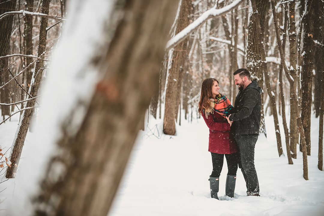 a newly engaged couple in the snowy woods laughing