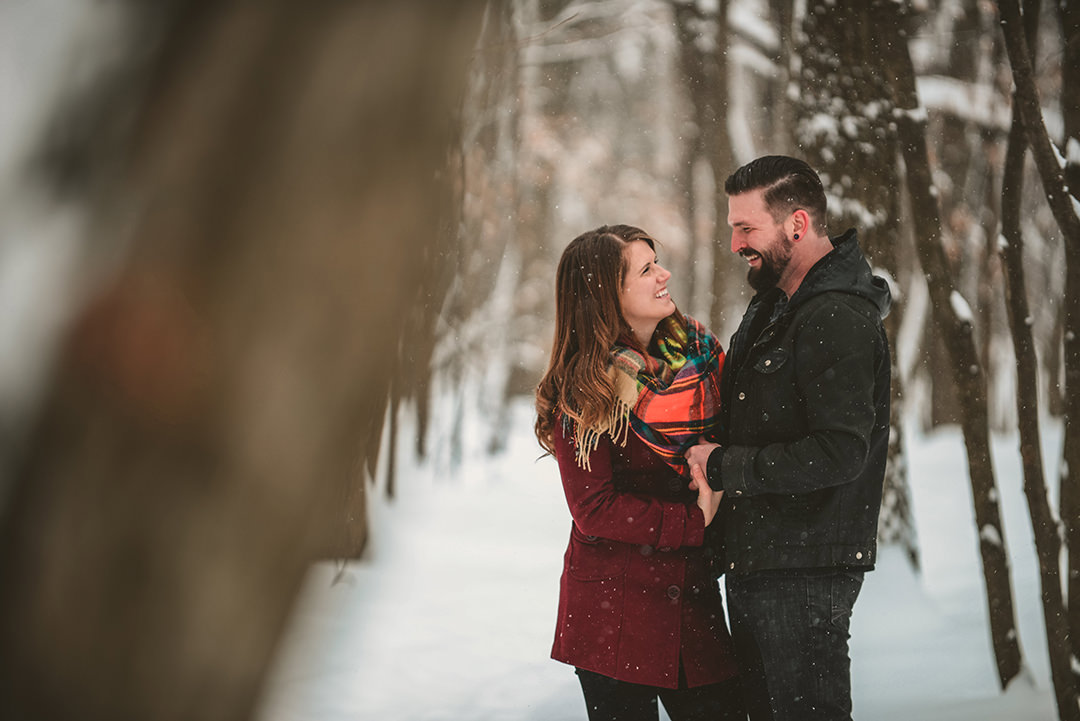 an engaged couple laughing in the snowy woods