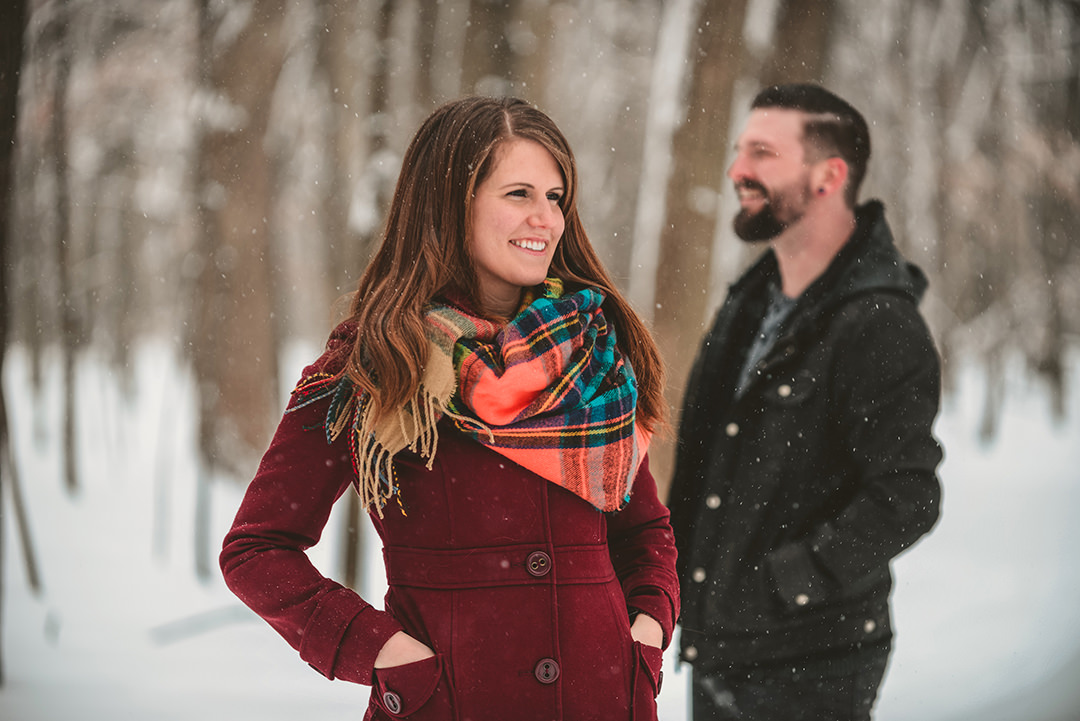 a newly engaged couple standing in the woods as it snows