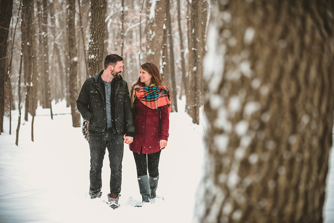 a newly engaged couple walking in the snowy woods as they laugh
