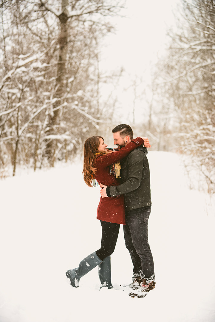 a engaged couple throwing their arms around each other as they stand in the snow