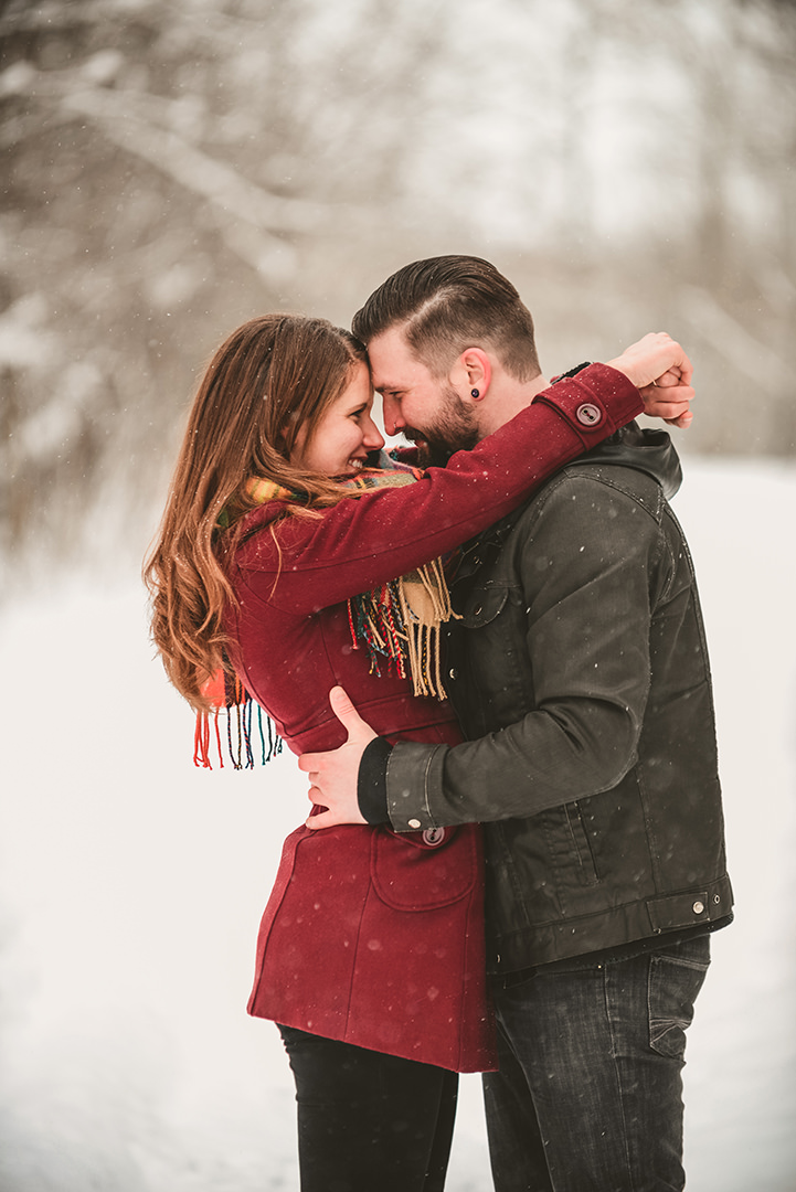 a man and a woman touching heads as they smile in the snow