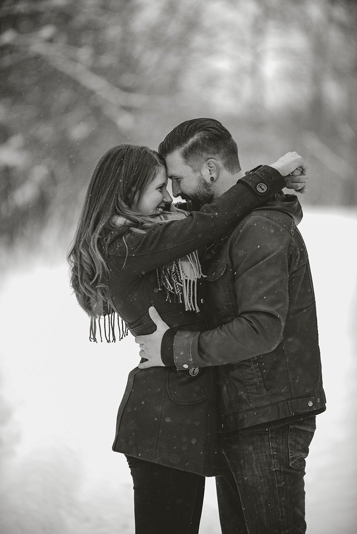 a newly engaged couple laughing as they throw their arms around each other in the snow