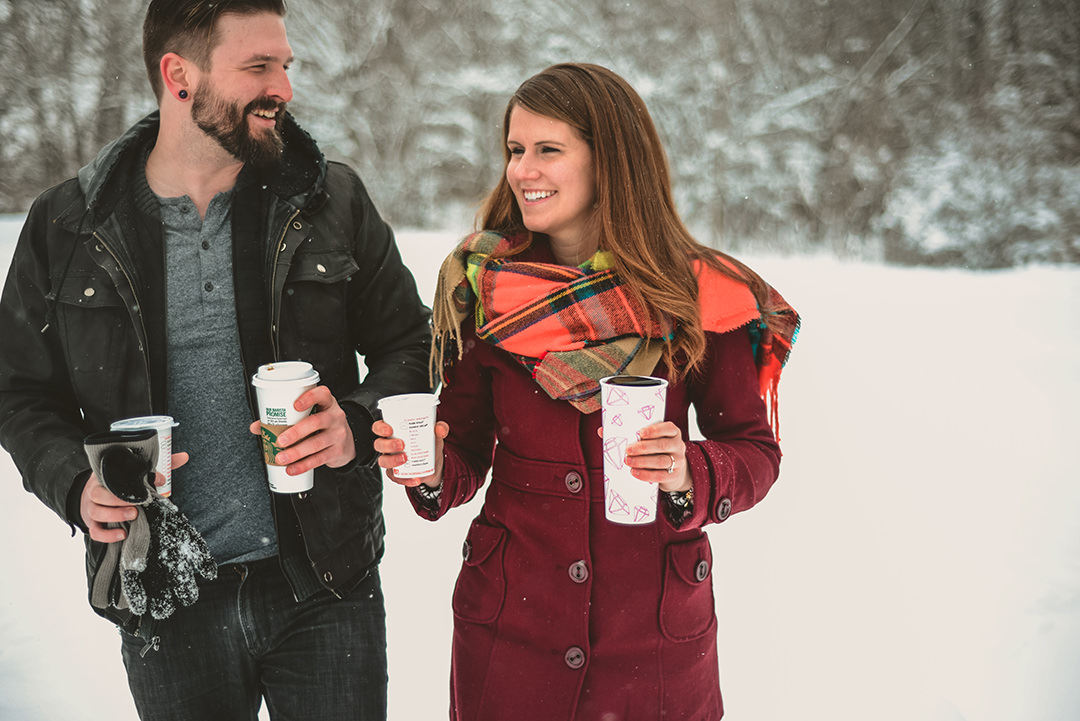a man and a woman carrying coffee as they laugh in the snow