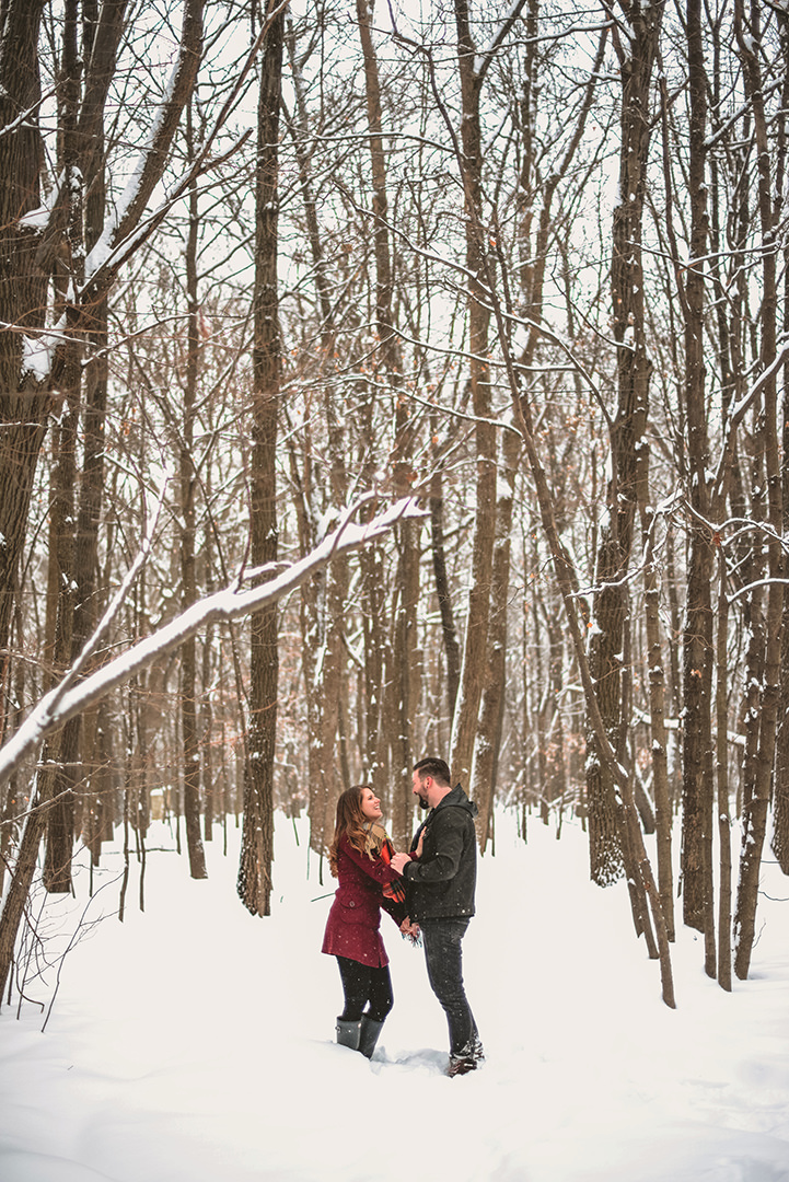 a newly engaged couple laughing in the snowy woods in the morning