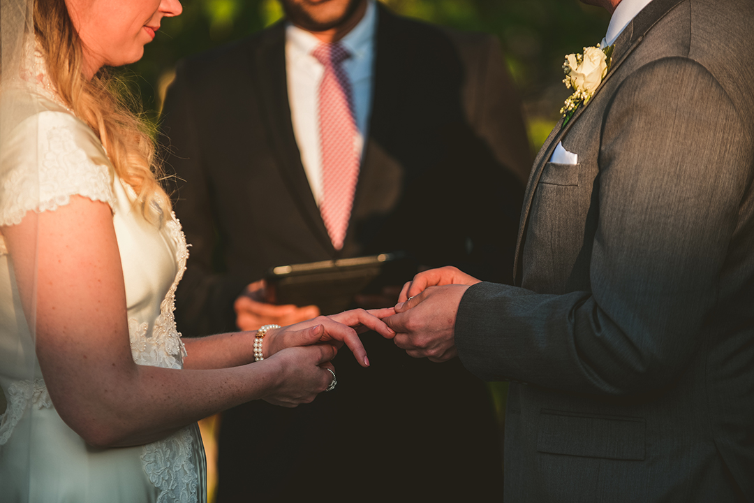 the groom putting the ring on the brides hand during an evening wedding ceremony