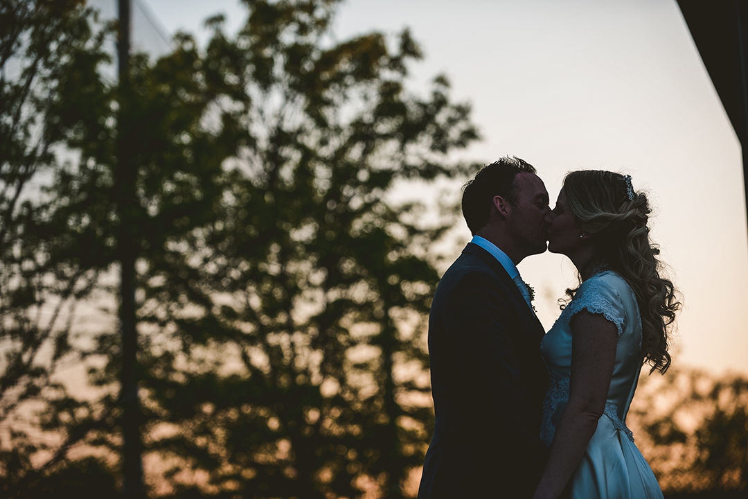 a silhouette of a bride and groom kissing in front of the sunset