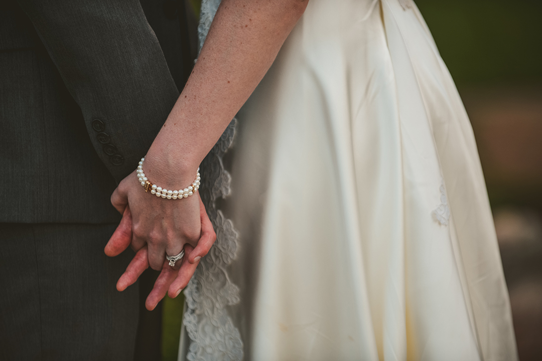 a detail of the bride and groom holding hands in the evening