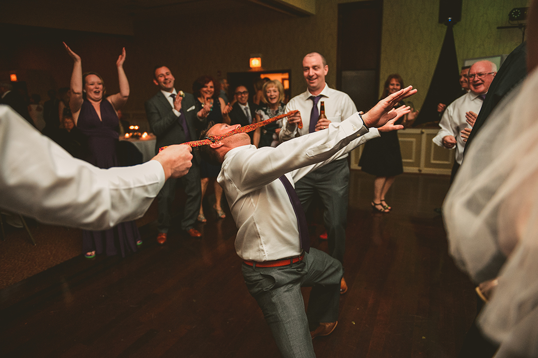 a man limboing under a tie at a wedding reception