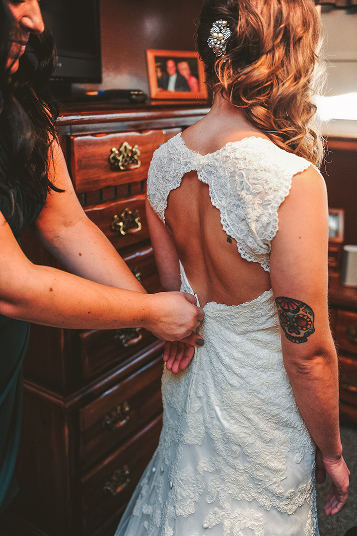 the maid of honor zipping up a tattooed bride