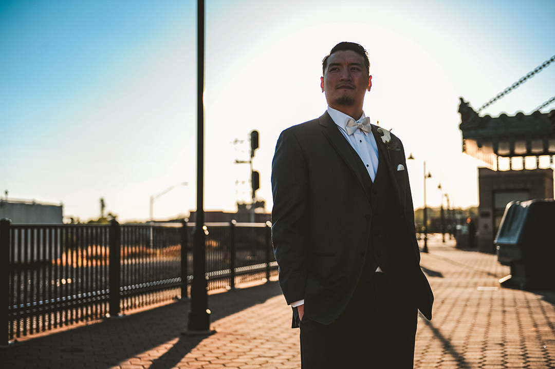 a groom standing with his hands in his pocket with a strong backlight