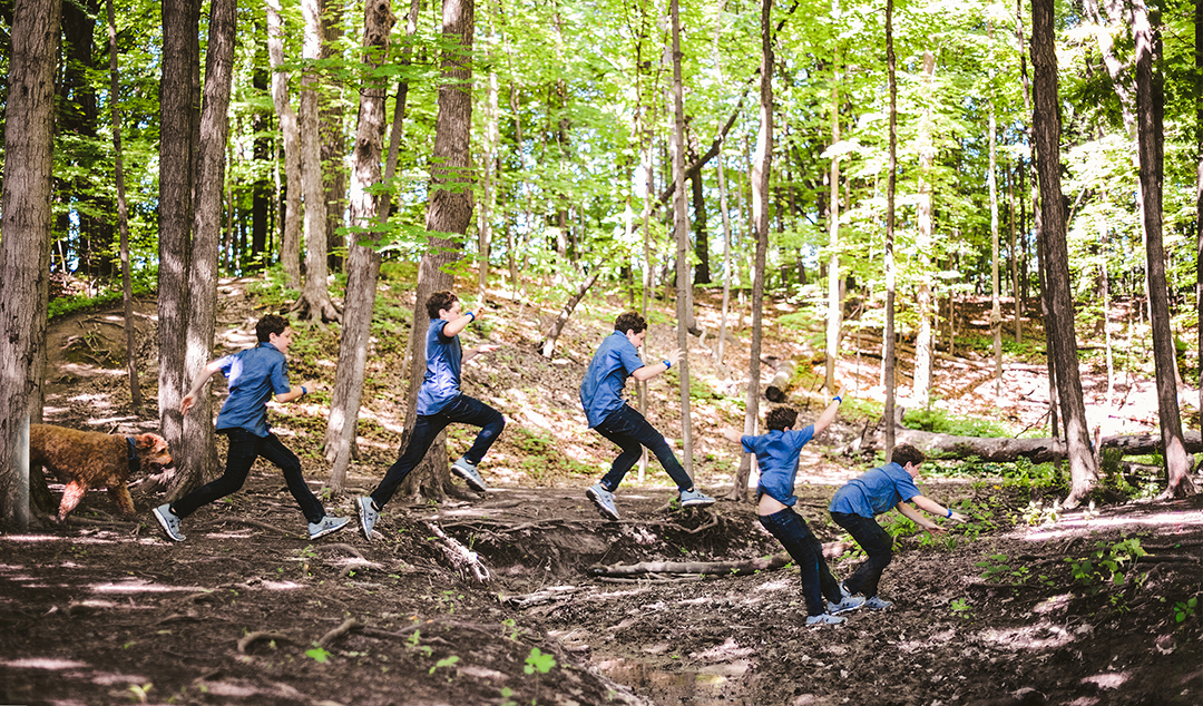 a boy jumping across a creek at an engagement session in the woods