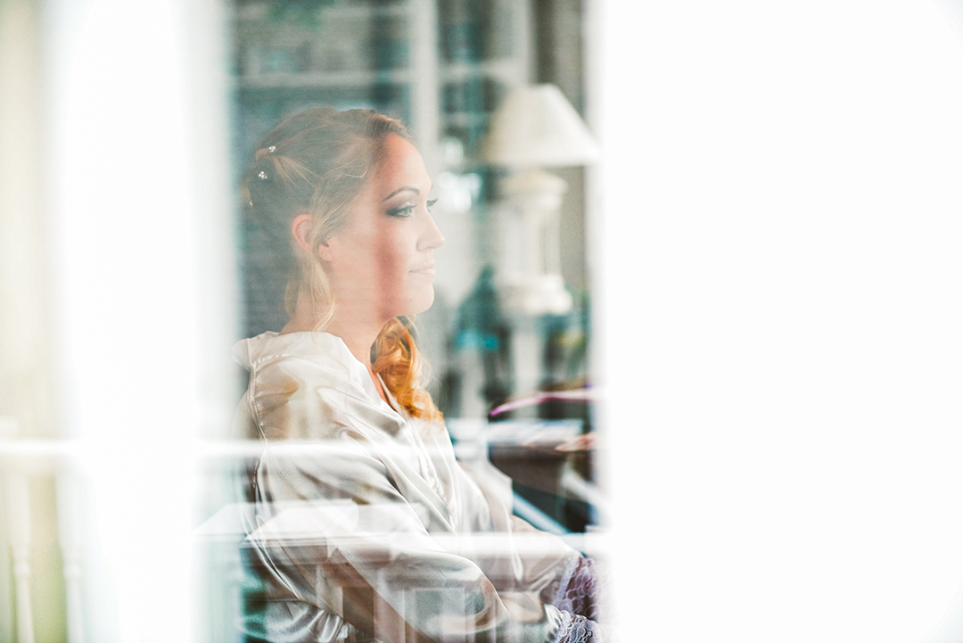 through the window of a bride getting her makeup applied by a professional makeup artist