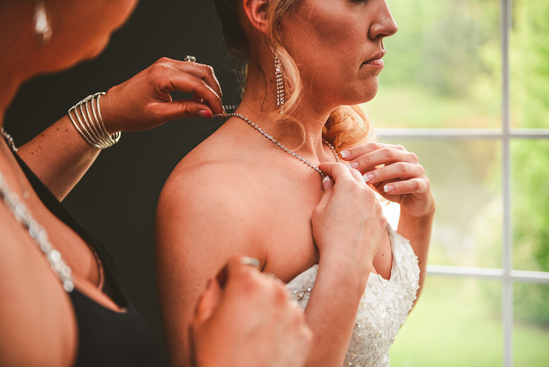 the made of honor putting on the brides necklace on her wedding day