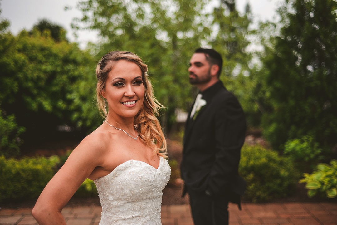 a bride smiling as her groom stands in the background