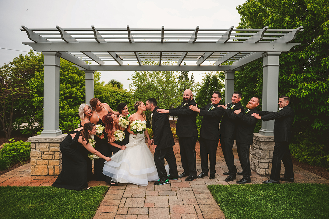 a bridal party pulling apart the bride and groom as they try to kiss