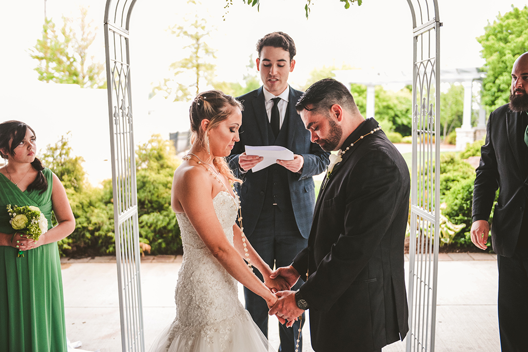 the bride and groom with their eyes closed with a rosary draped around them as they hold hands