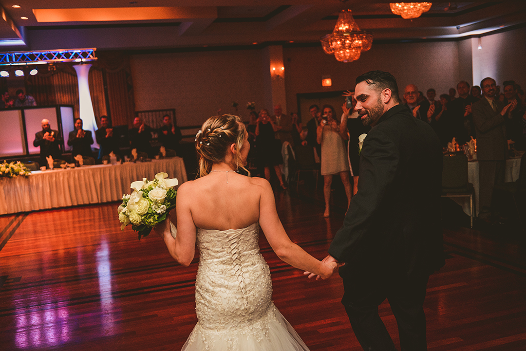 the bride and groom entering their reception with everyone clapping