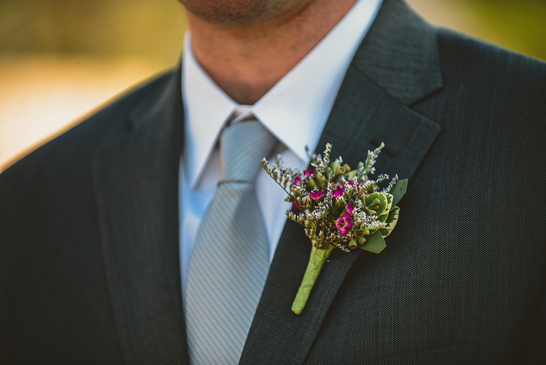 a purple and white boutonnière on a groom lapel