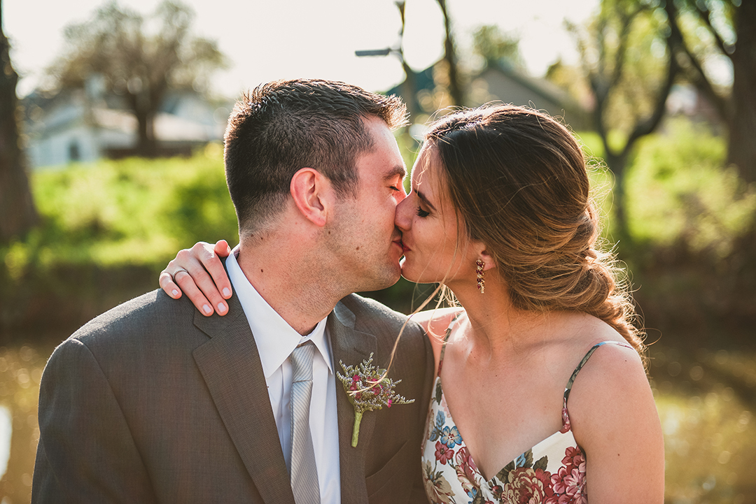a bride and groom kissing with the setting sun in the background