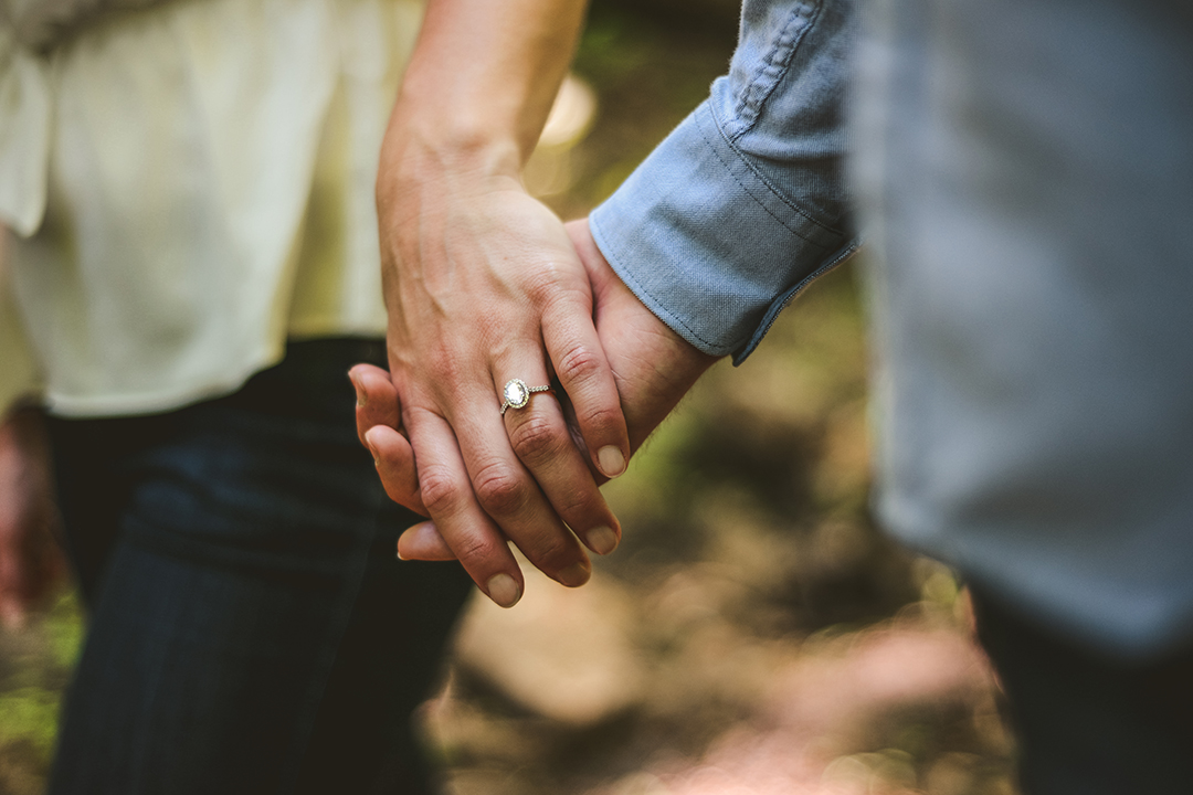 a detail of a man and a woman holding hands with their engagement ring showing