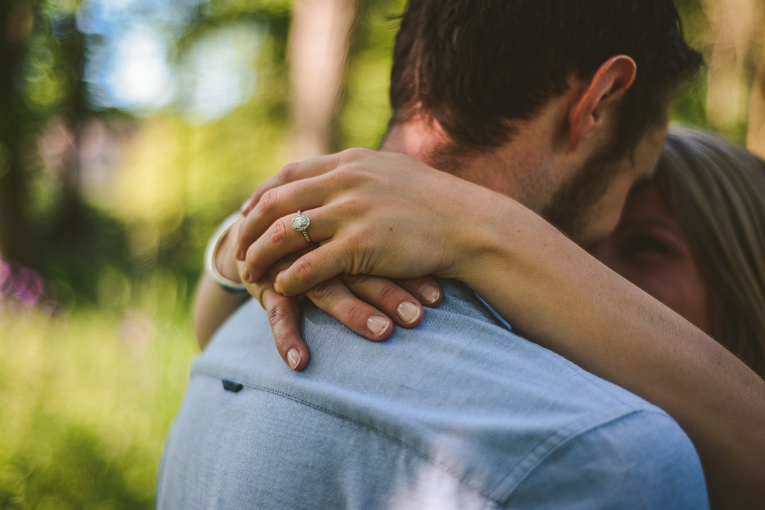 details of a womans arms around her boyfriend in the woods showing off her engagement ring