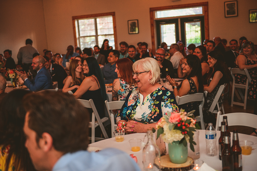 the mother of the bride laughing during the best man speech as everyone around her also laughs and claps